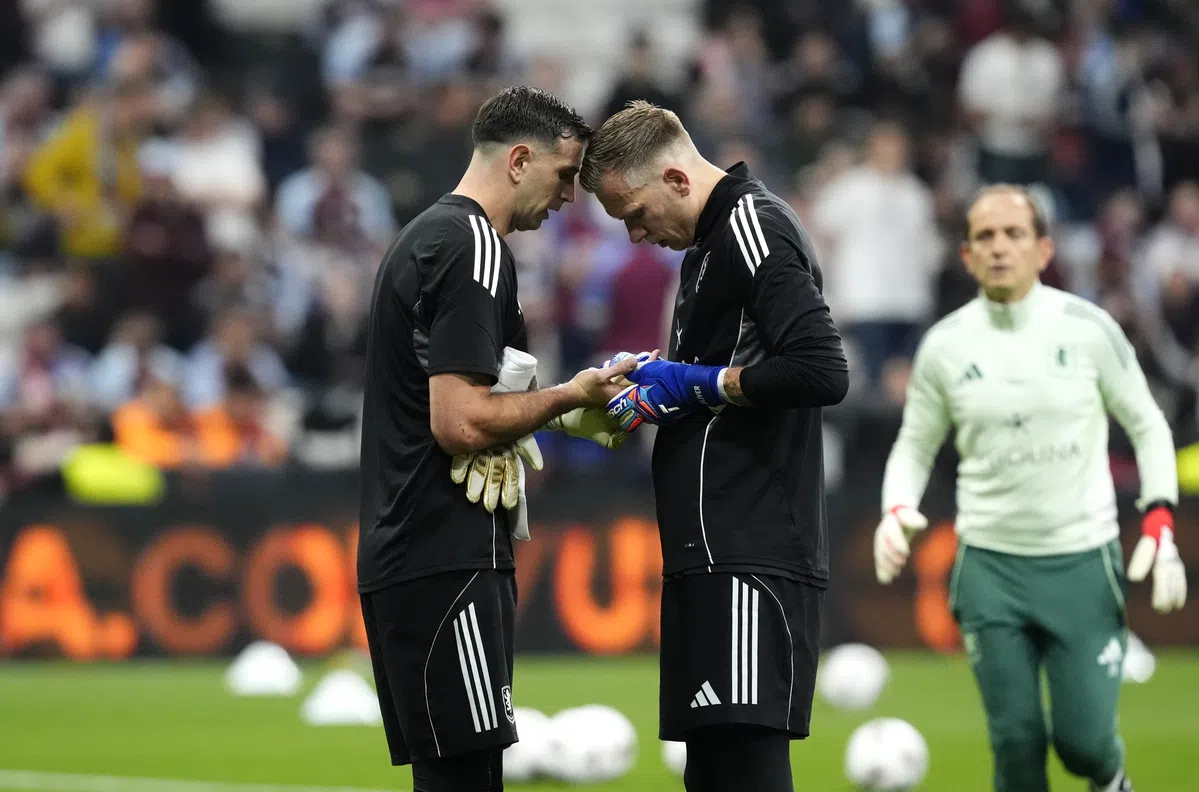 Emiliano Martínez celebrating with the Europa League trophy after Aston Villa's victory, possibly with his finger taped or visibly in discomfort.