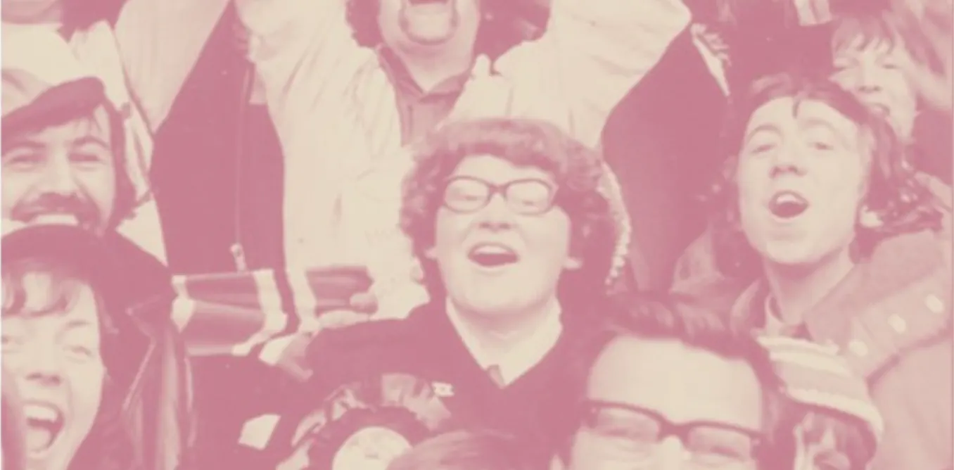 A group of diverse women football fans cheering at a stadium, some wearing scarves, with an exhibition display in the background showcasing historical photos of female supporters.
