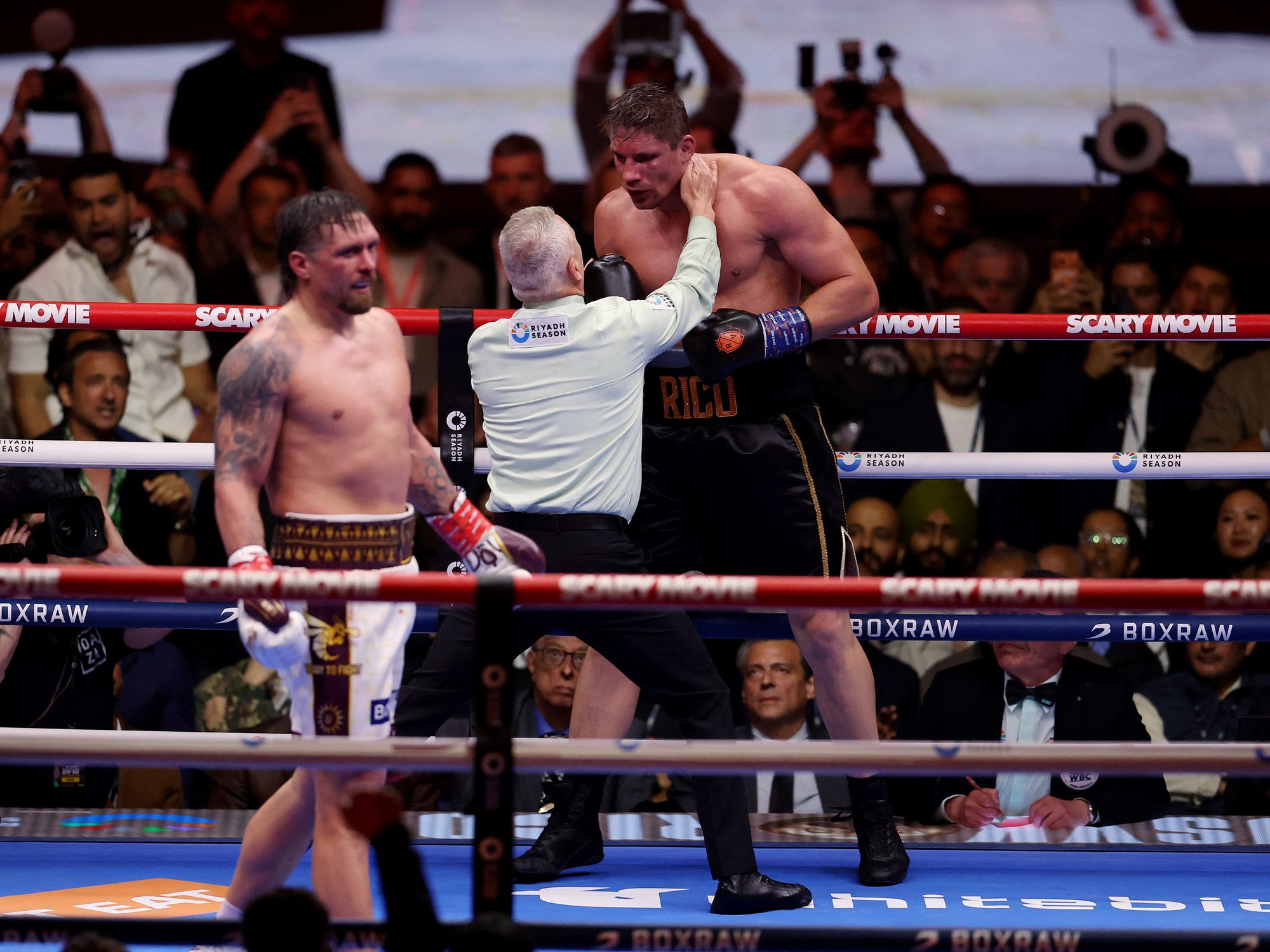 Oleksandr Usyk and Rico Verhoeven grappling in the boxing ring.