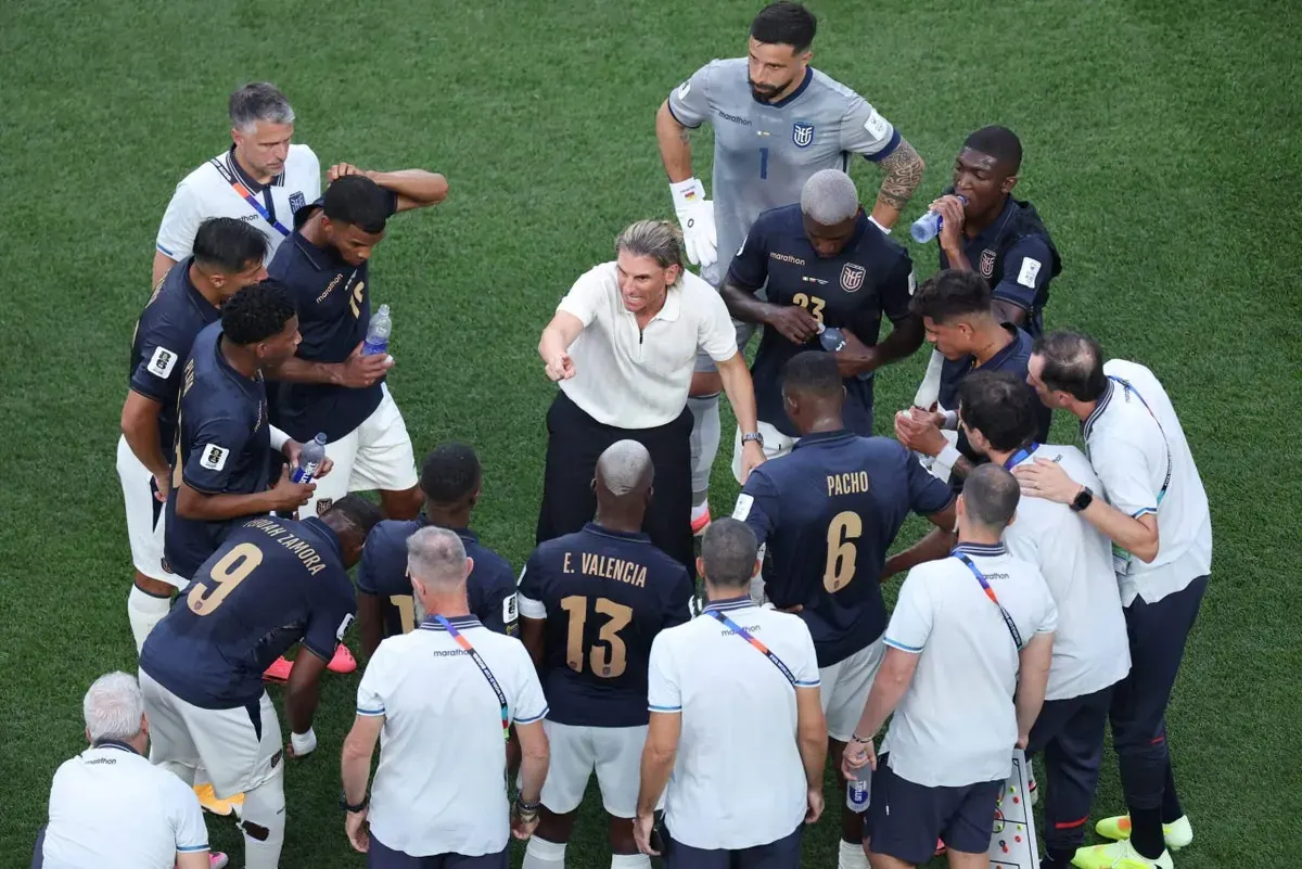 A World Cup coach consults with players on the pitch during a hydration break.