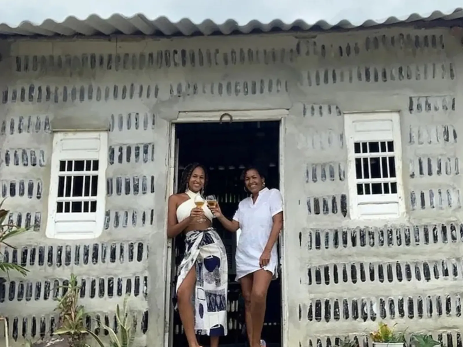 A mother and daughter working on the construction of a house made from thousands of green and clear glass bottles.