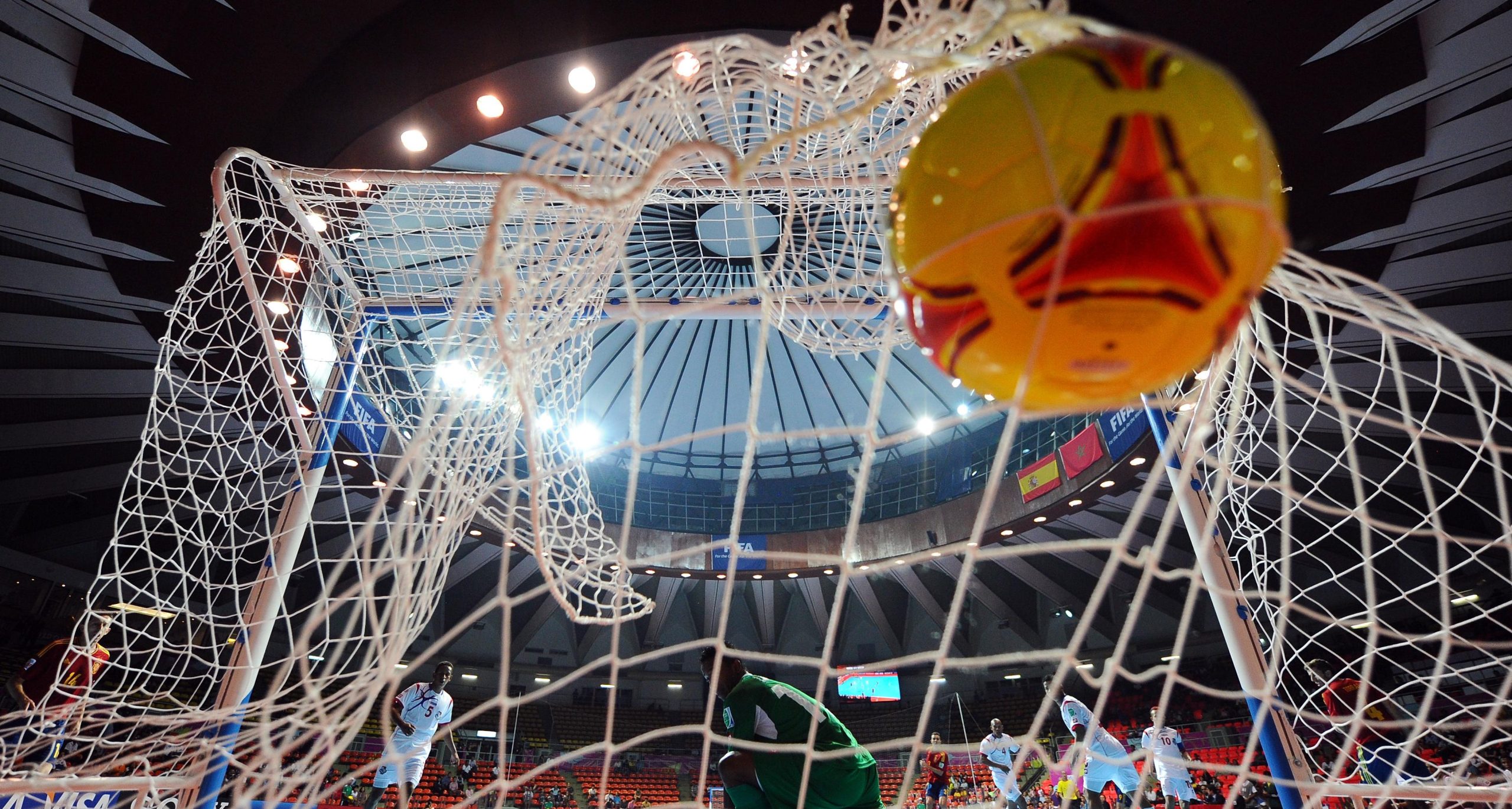 Futsal players engaged in a training drill on an indoor court, with coaches observing.