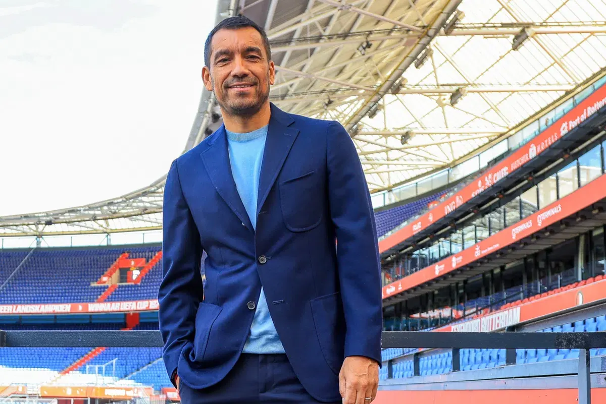 Giovanni van Bronckhorst speaking at a Feyenoord press conference in De Kuip stadium, wearing a Feyenoord training jacket, July 2026
