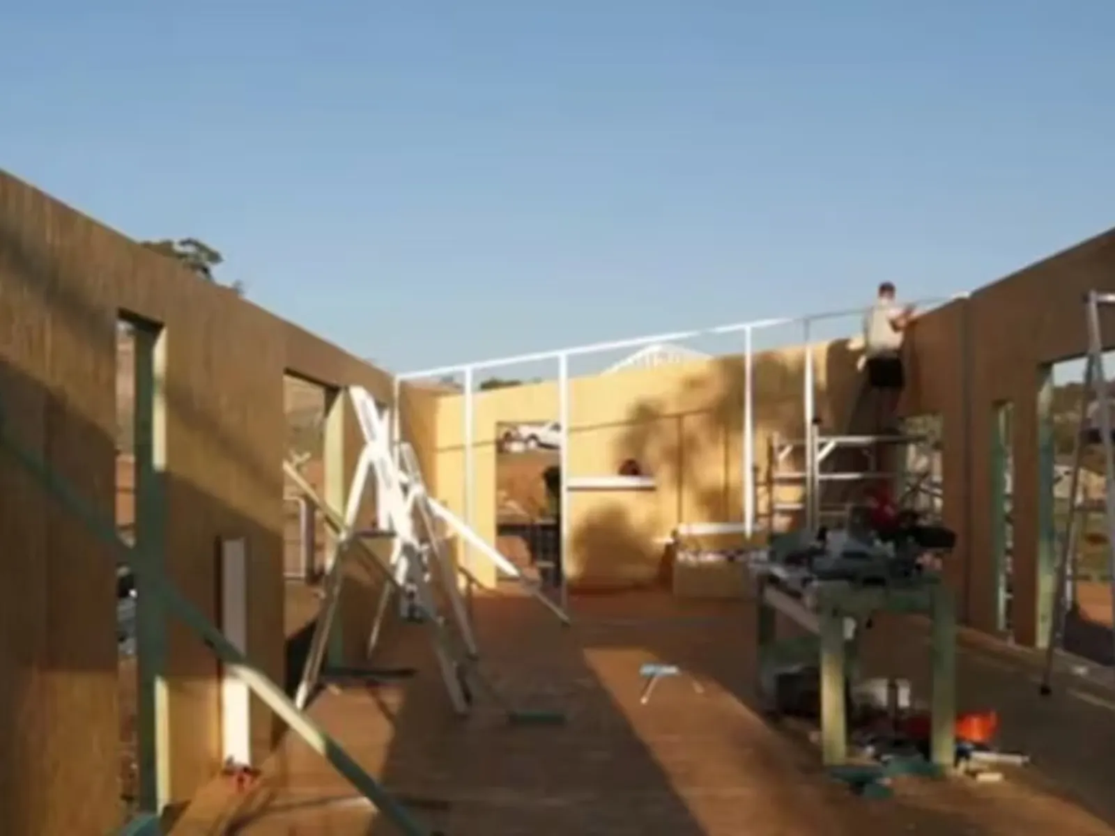 A modern, eco-friendly house in a rural landscape, with solar panels visible on the roof.