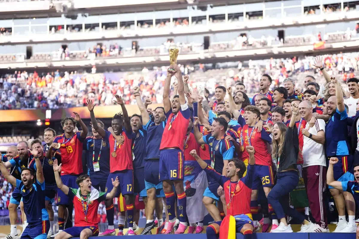 Spain national football team captain Rodri lifting the FIFA World Cup trophy with teammates celebrating on the pitch.