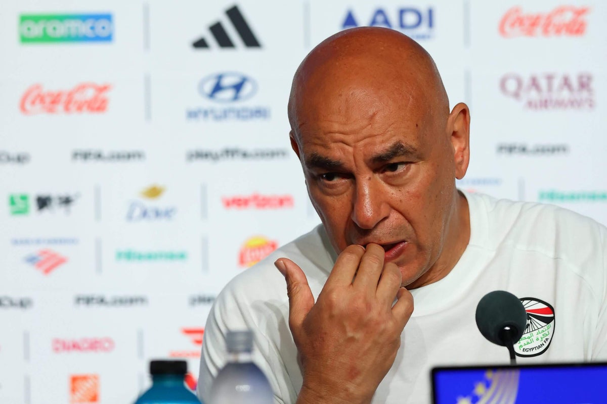 Egypt national football team coach Hossam Hassan speaking at a press conference, with a Palestinian flag visible.