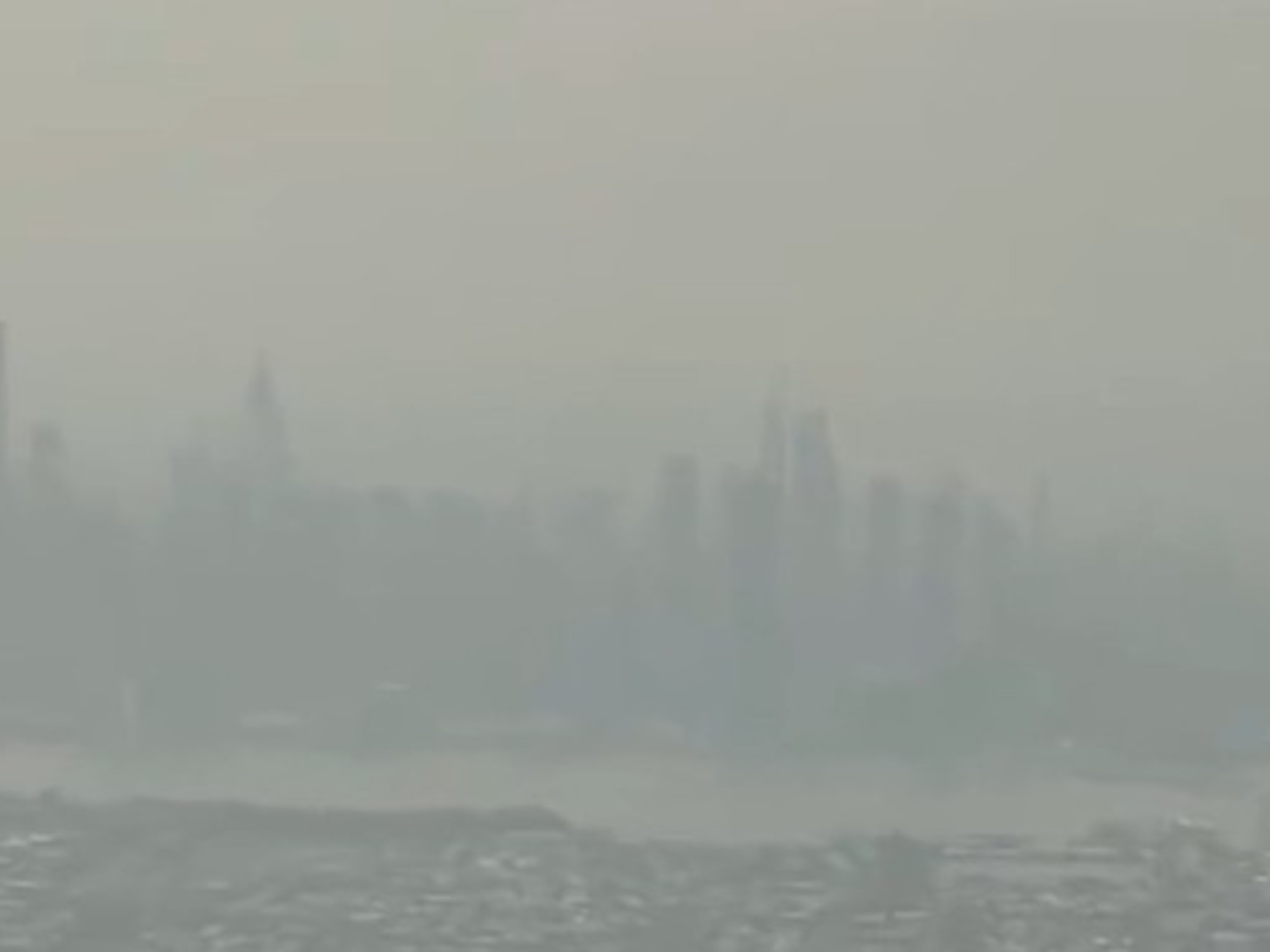 The New York City skyline is shrouded in a hazy, grey-brown layer of smoke, significantly reducing visibility.