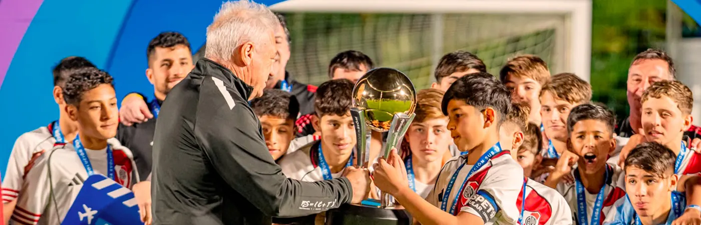 Youth football players celebrating with trophies at the Fiesta CONMEBOL Evolución awards ceremony.